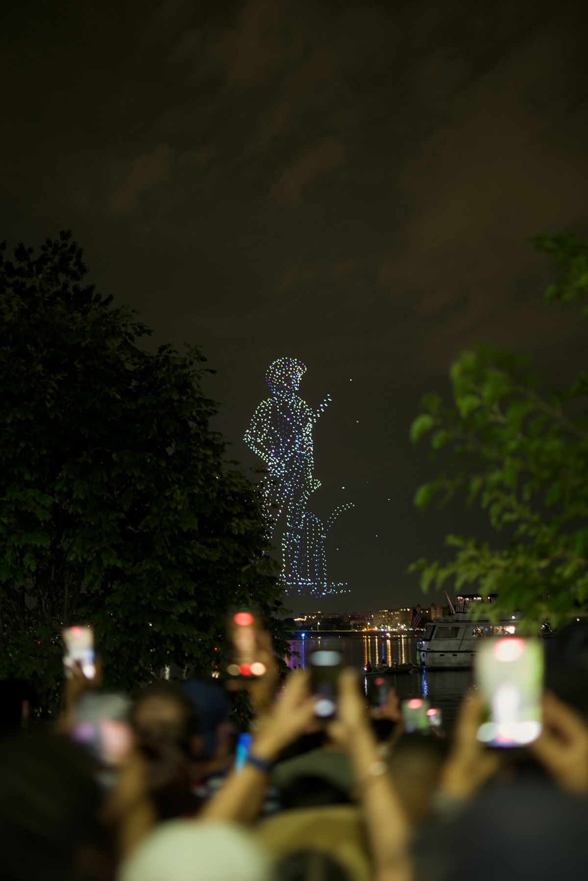Publiek kijkt naar een droneshow die een figuur vormt in de lucht